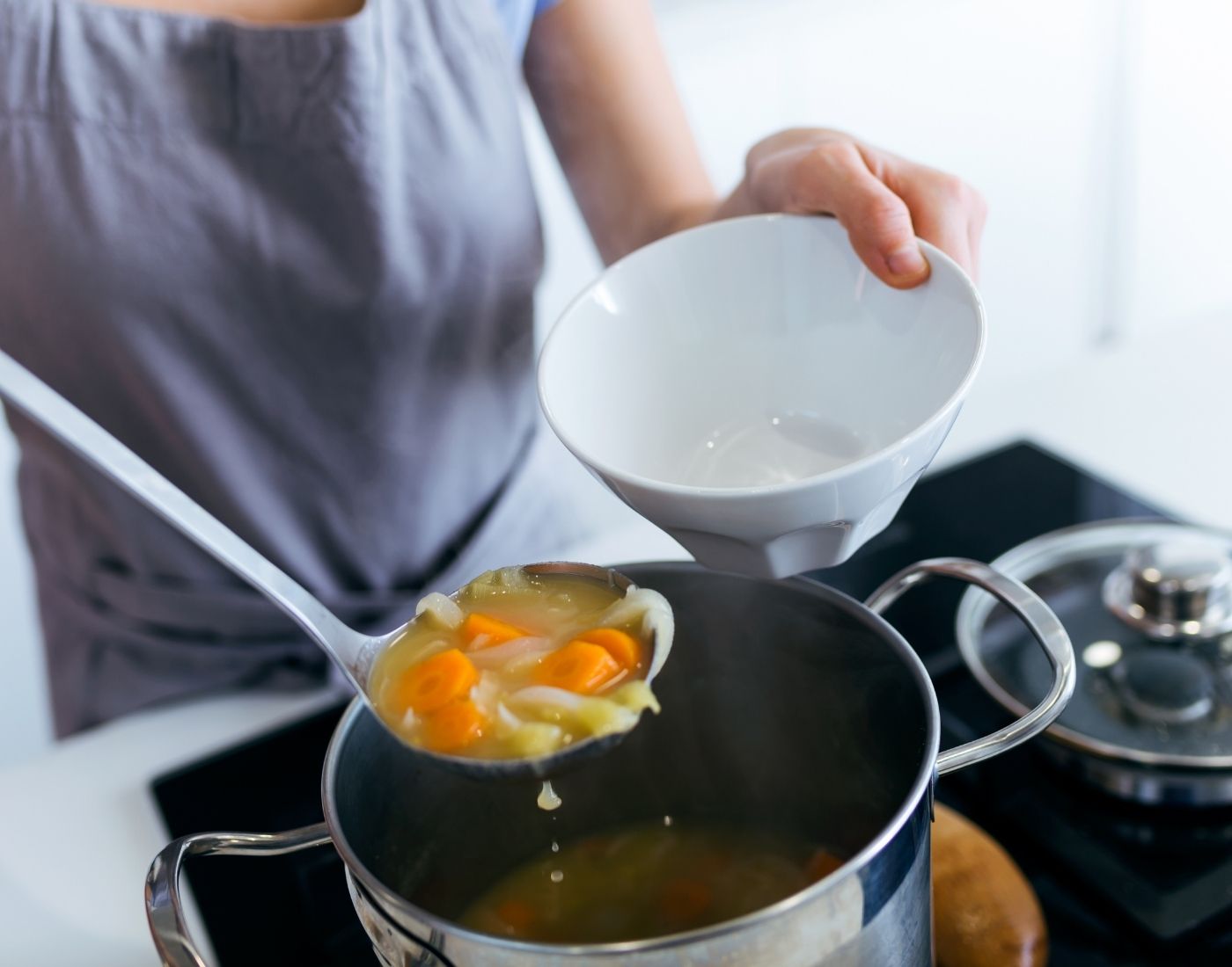 Person ladling homemade soup with celery and carrots into a bowl from a large pot on the stove