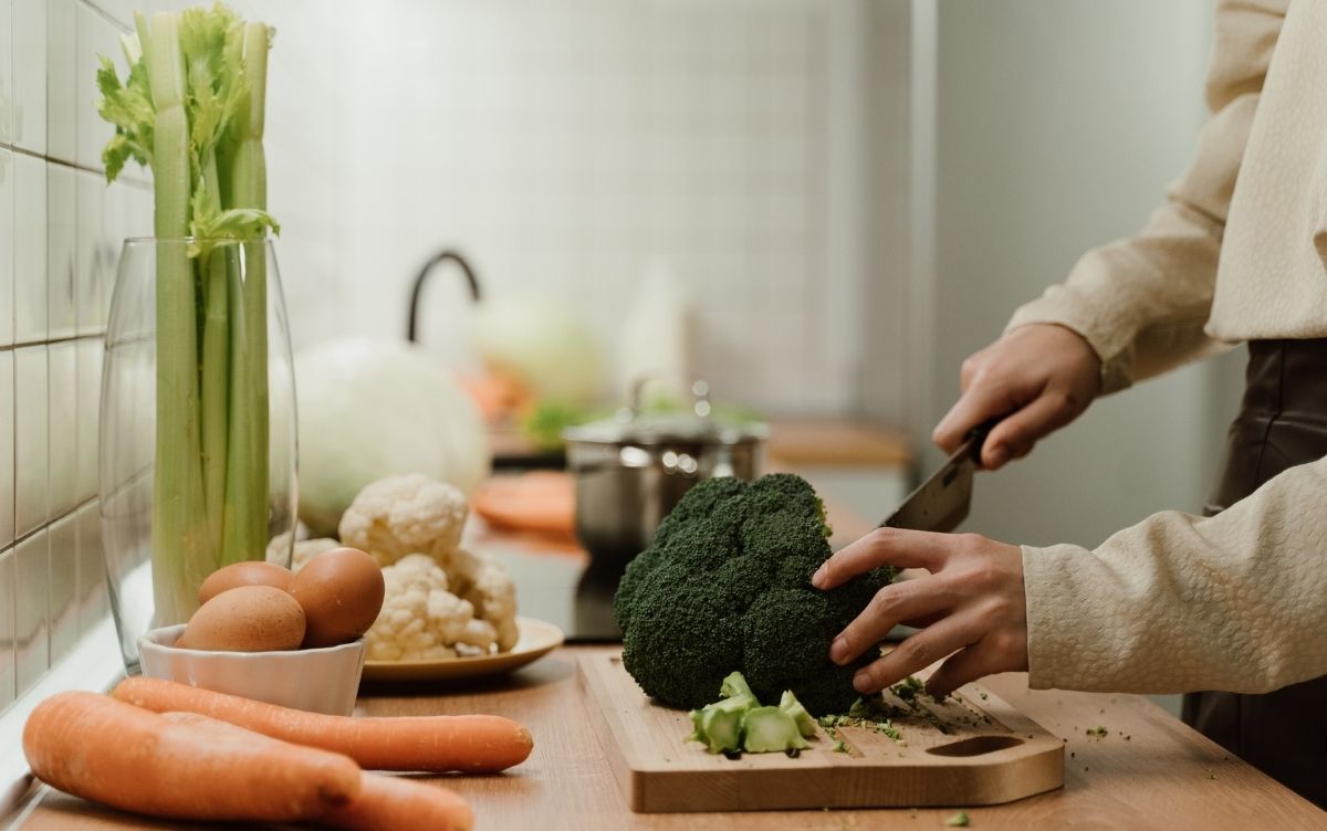 Person cutting broccoli on a chopping board with other food types, including major allergens like celery and eggs, kept separate