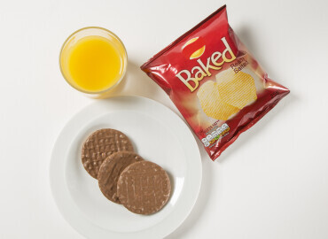image showing a glass of fresh orange juice with a packet of crisps and chocolate digestives