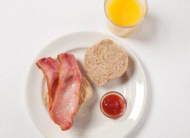 Photo of a bacon roll with tomato ketchup and a glass of fresh orange juice