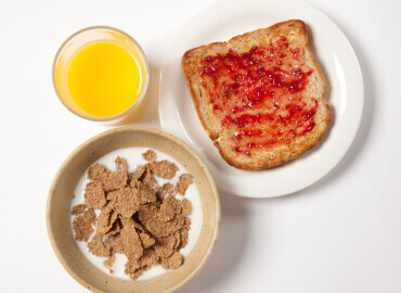 Photo of a bowl of wholegrain breakfast flakes, slice of wholemeal toast and jam, and glass of fresh orange juice