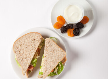 Photo of a cheese salad sandwich with a bowl of yogurt and dried fruit beside it