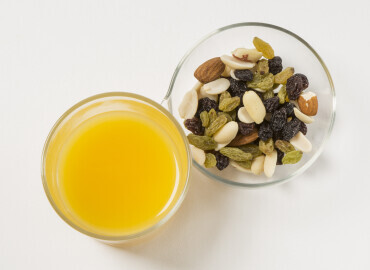 Photo of a glass of fresh orange juice, mixed nuts and raisins
