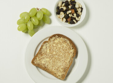Photo of mixed nuts, raisins, and grapes, slice of toast with lower fat spread