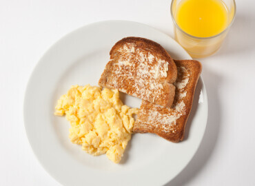 Photo of a plate of scrambled eggs, a slice of wholemeal toast and lower fat spread, and a glass of fresh orange juice