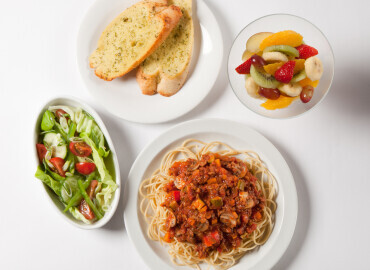 Photo of spaghetti bolognese with garlic bread, a side salad and a fruit salad