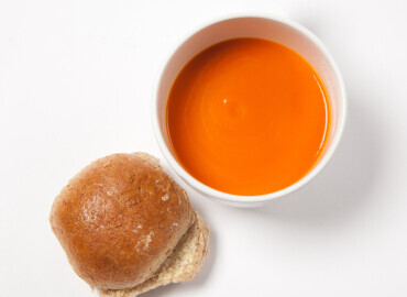 Photo of a bowl of tomato soup with a bread roll
