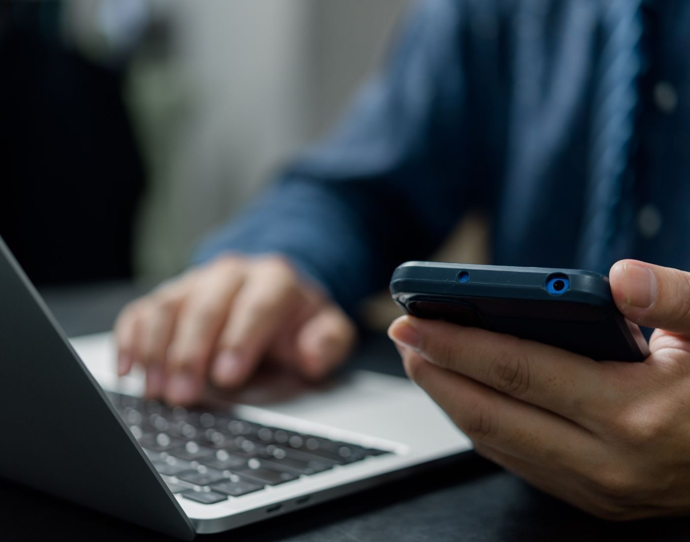 Close-up of a man using a laptop trackpad while holding a smartphone