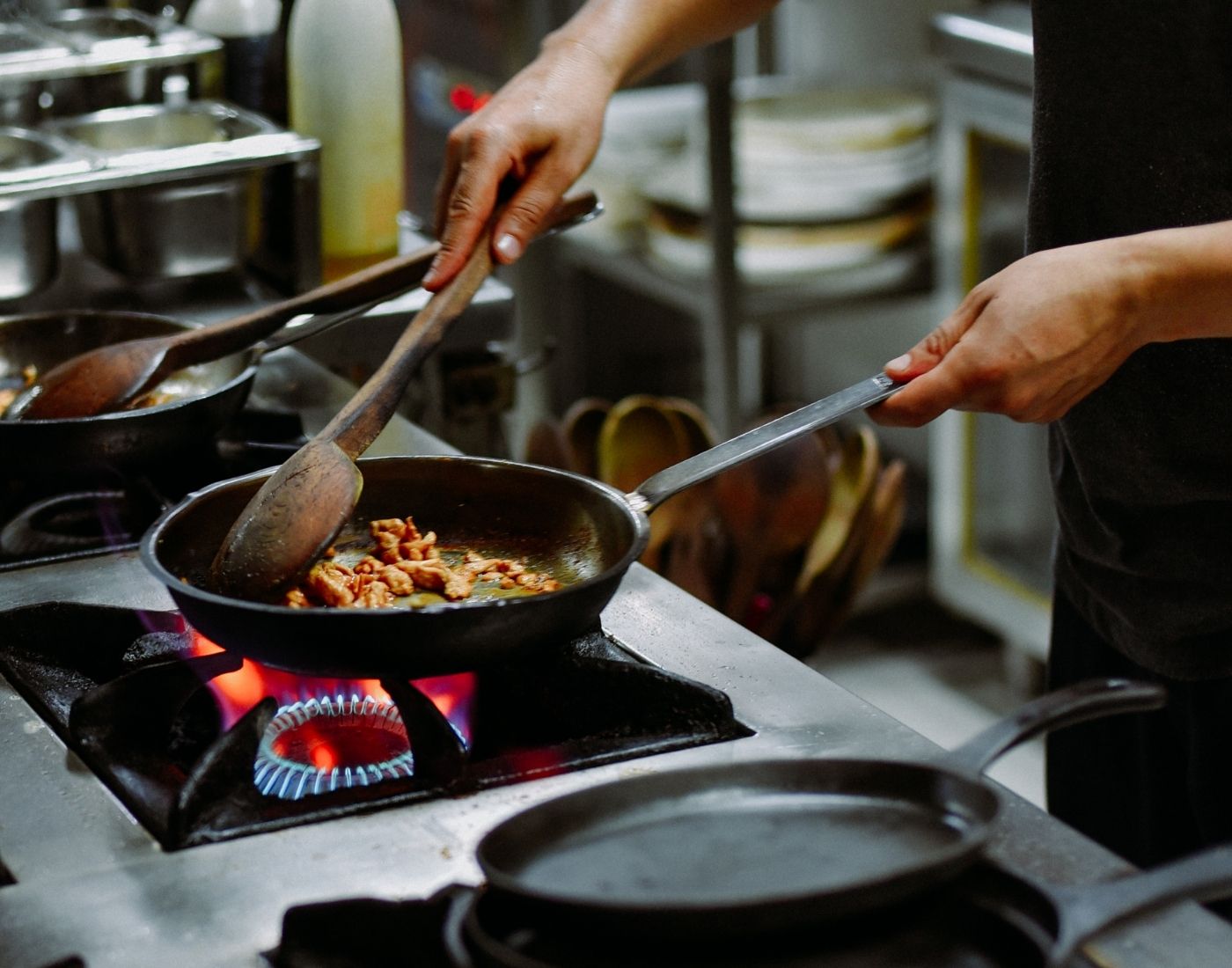 Worker in professional kitchen cooking poultry in frying pan