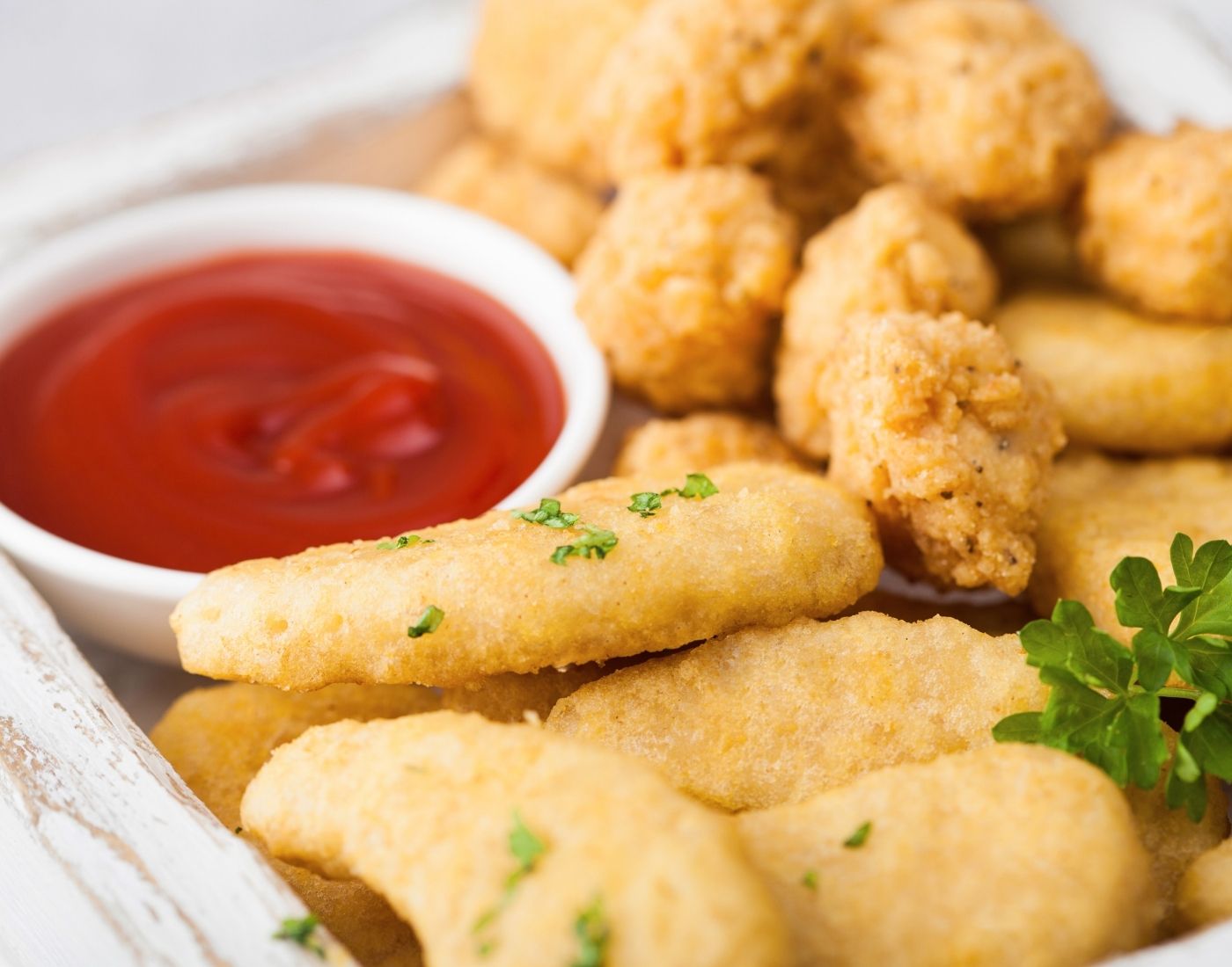 A close-up image of breaded chicken nuggets and fish sticks served with a side of ketchup and garnished with parsley.