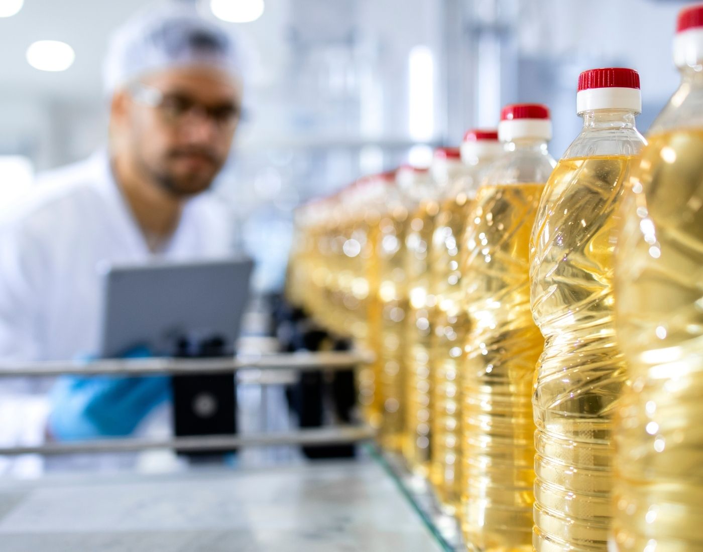 Quality control worker inspecting bottles of cooking oil on a production line in a factory.