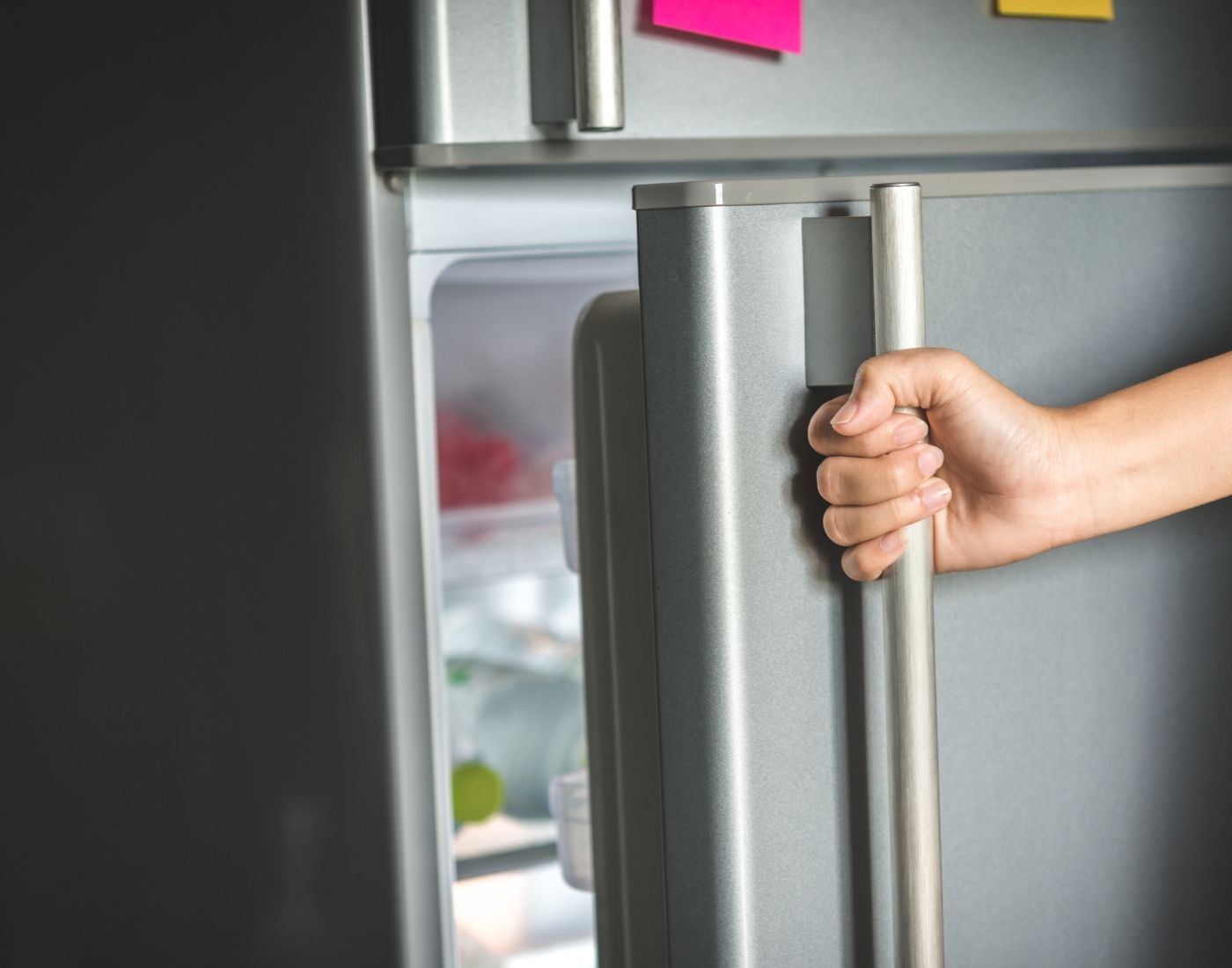 A person opening a stainless steel refrigerator door, revealing a glimpse of the contents inside.