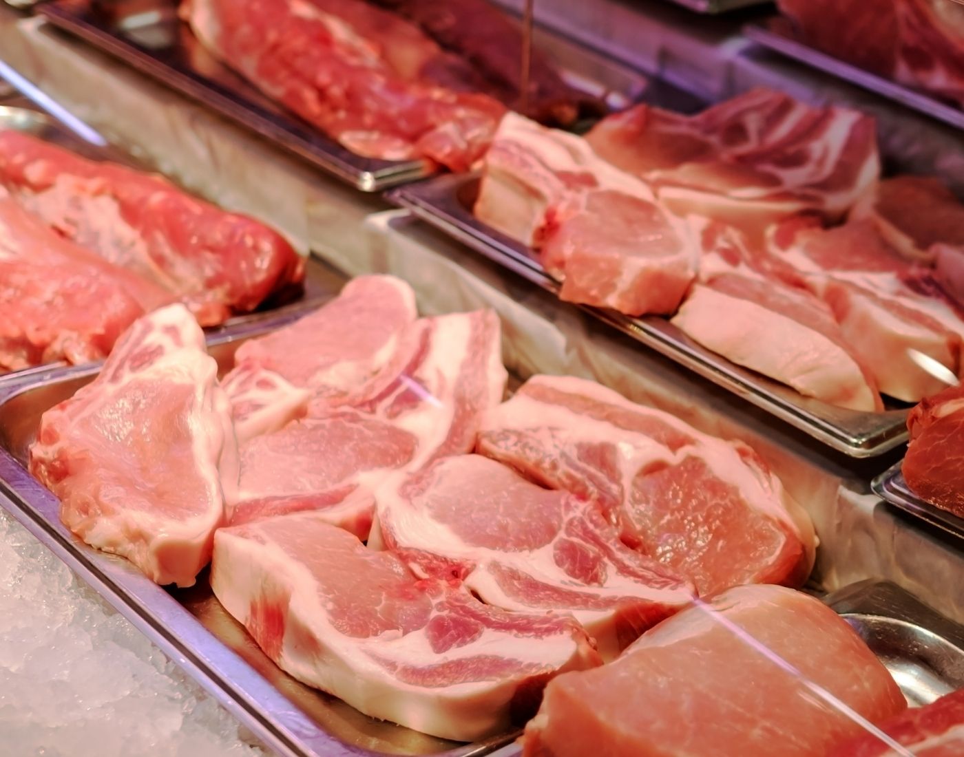Raw pork cuts displayed on trays in a well-lit supermarket or butcher shop