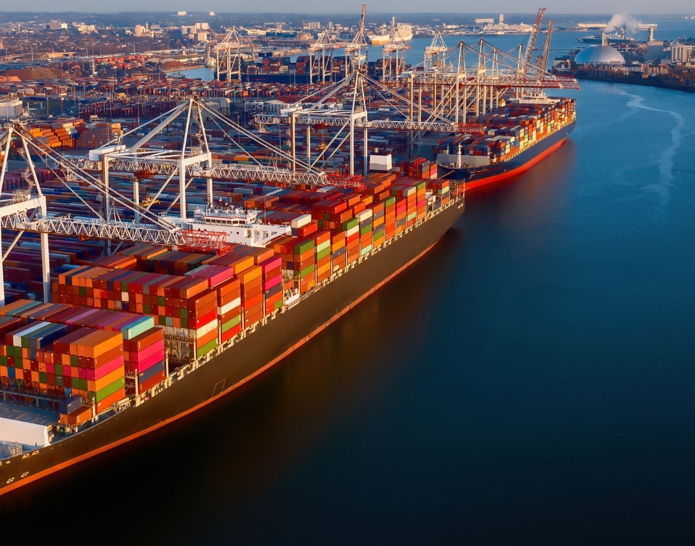Two cargo ships docked at a busy port, surrounded by cranes and colourful shipping containers.