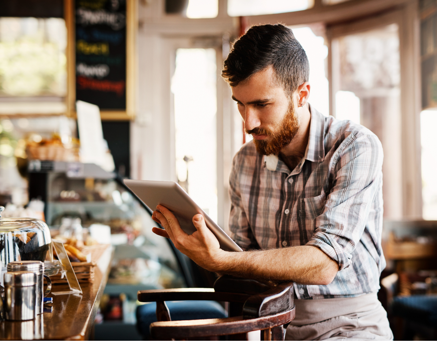 middle aged male member of staff in a cafe or coffee shop looks at a tablet possibly looking at guidance to run the business