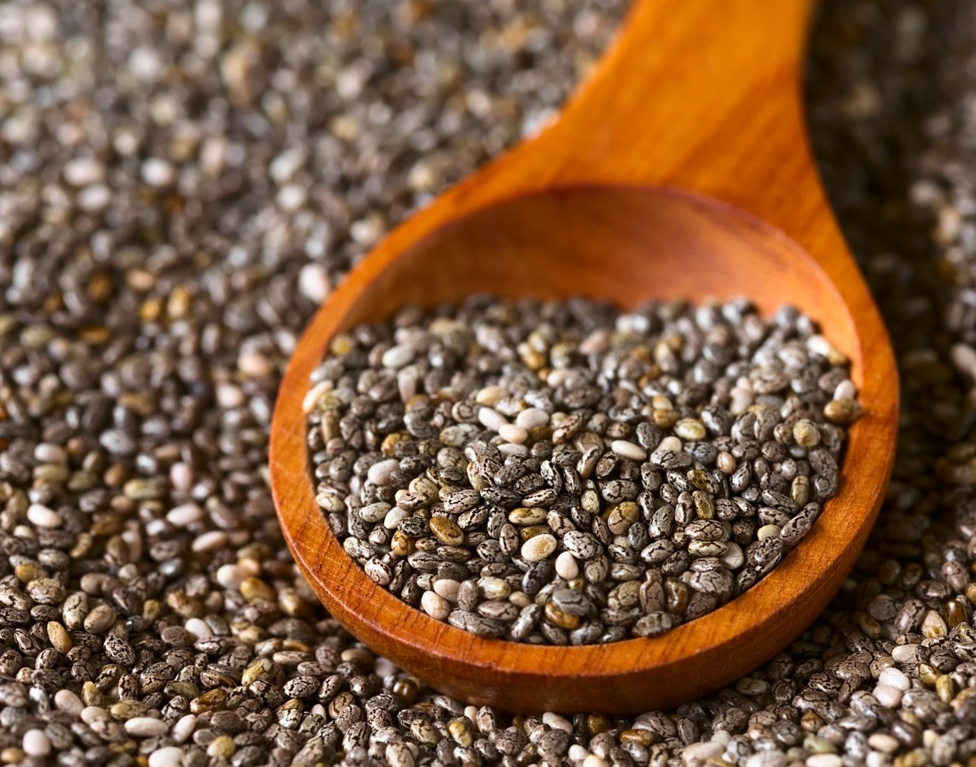 Chia seeds in a wooden spoon on top of more scattered chia seeds