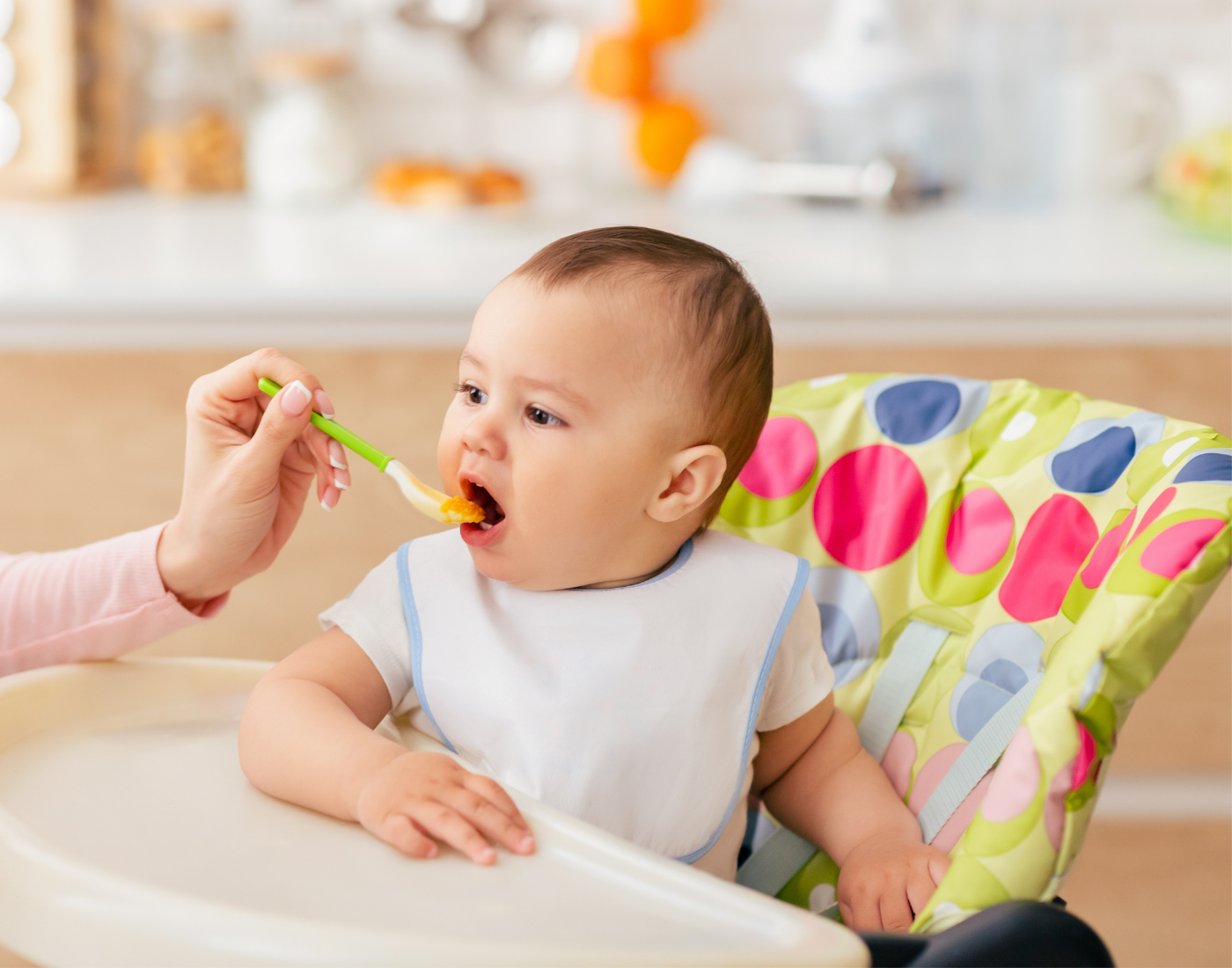 baby is given food from a spoon whilst sitting on a high chair