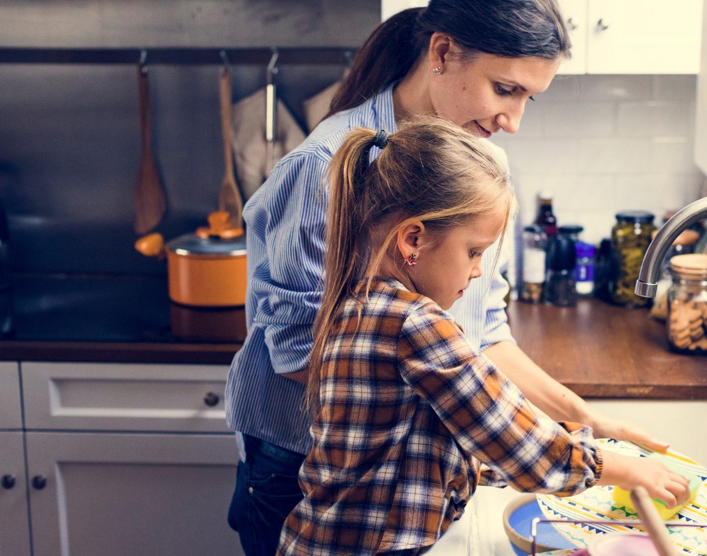 Mum and daughter standing at kitchen sink washing dishes
