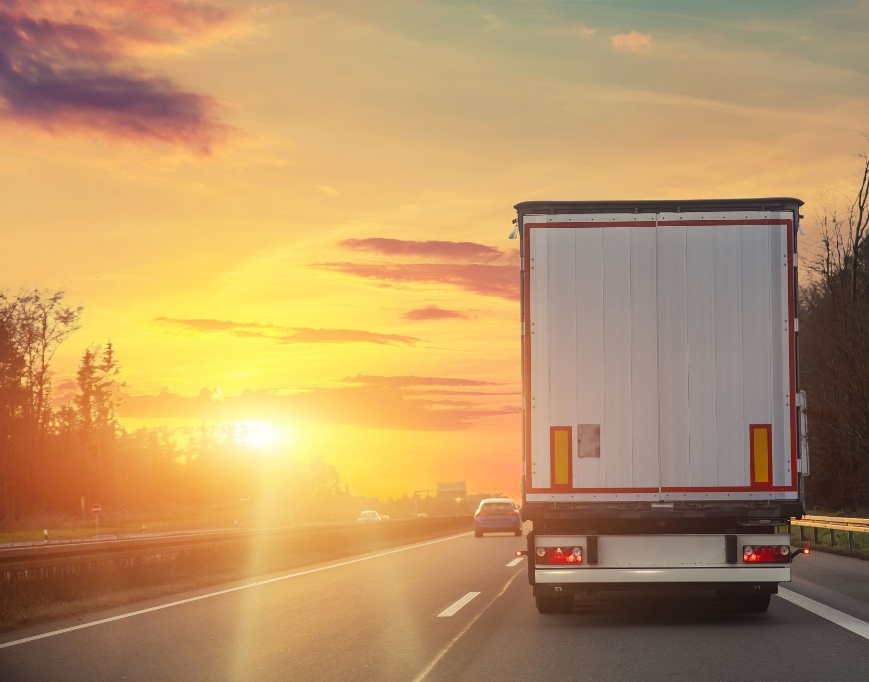 Back view of a large truck driving on a highway during sunset, with a warm-colored sky and other vehicles visible ahead