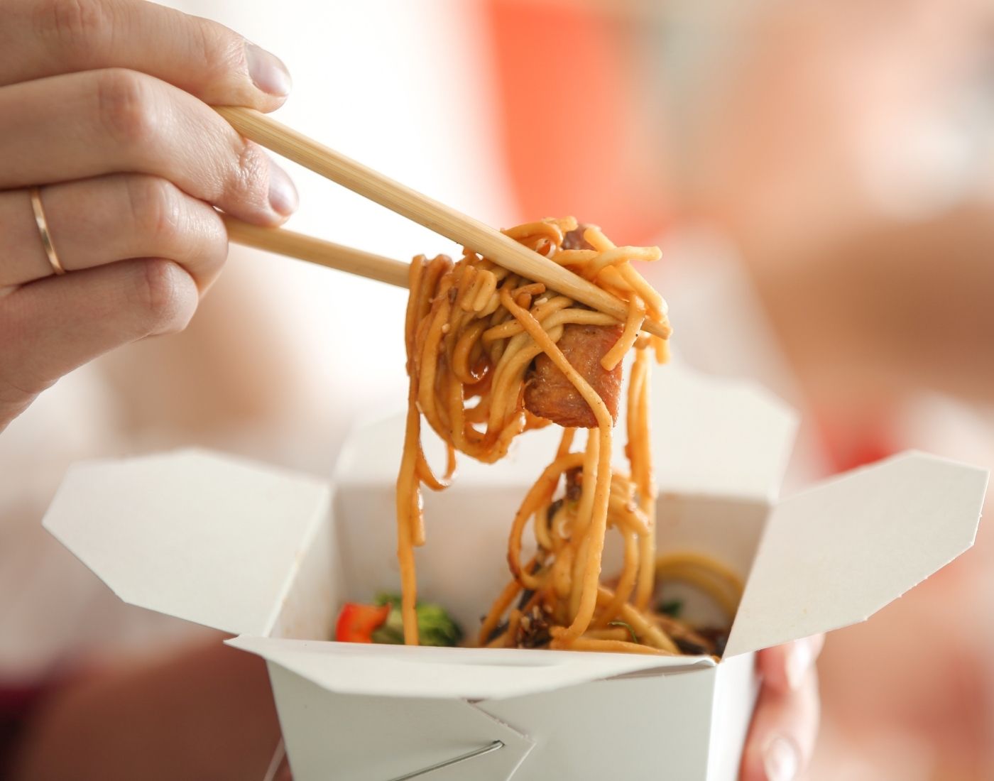 A person uses chopsticks to lift noodles from a takeout box.