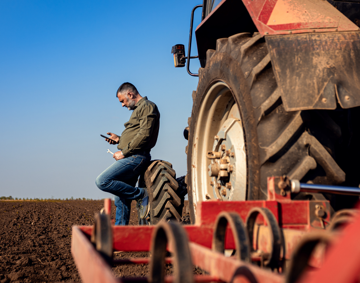 Farmer receives news on a phone while standing next to a tractor 