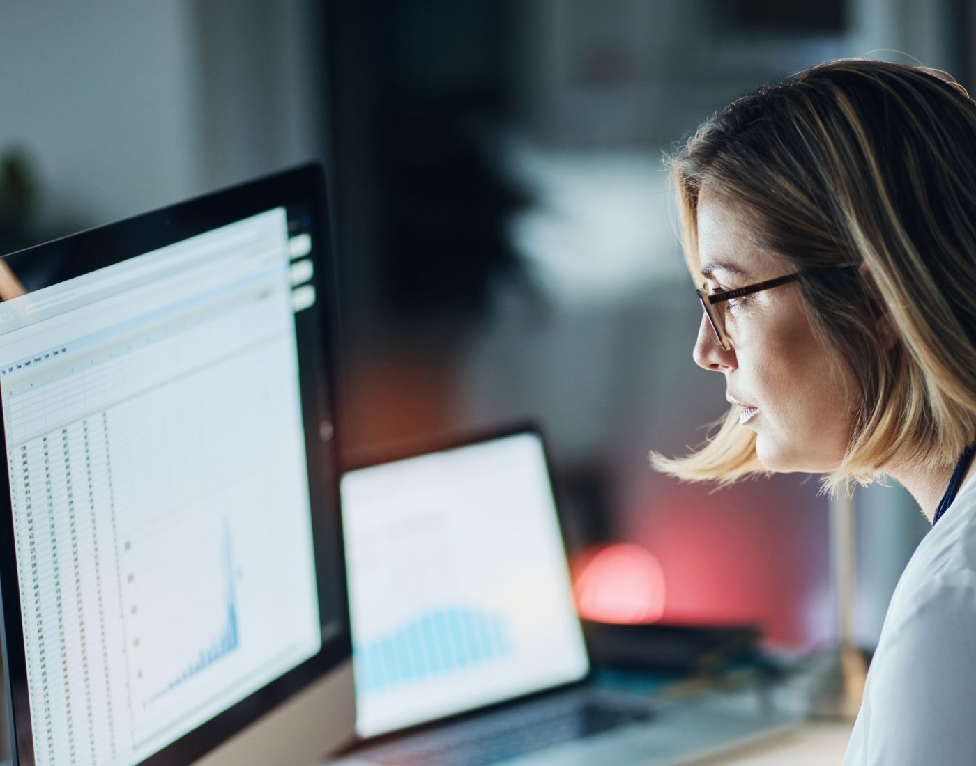 Female scientist wearing glasses sitting at a desk. She's looking at a computer monitor displaying data.