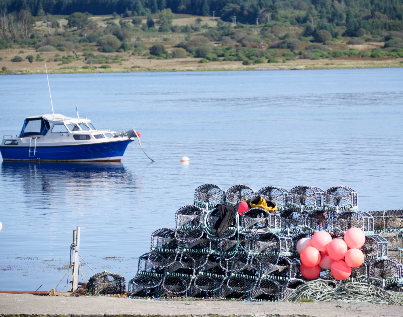 fishing boat on calm water loch with lobster nets on land.