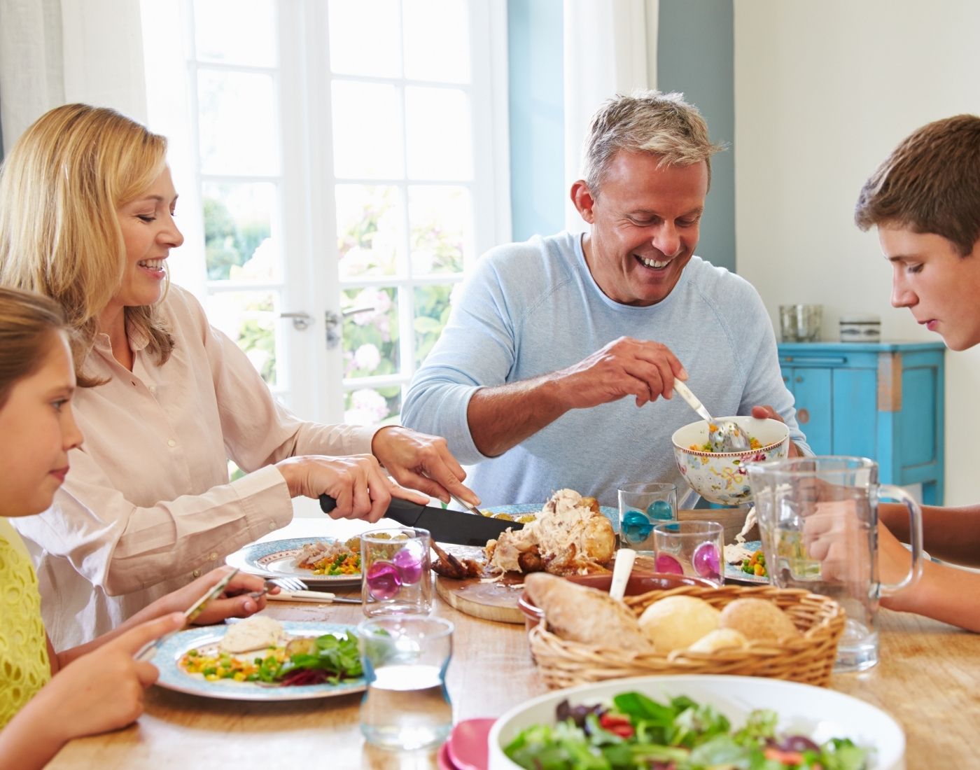 Mum, dad, teenage son and young daughter sitting at a table. They are eating a healthy meal of salad, chicken and bread.