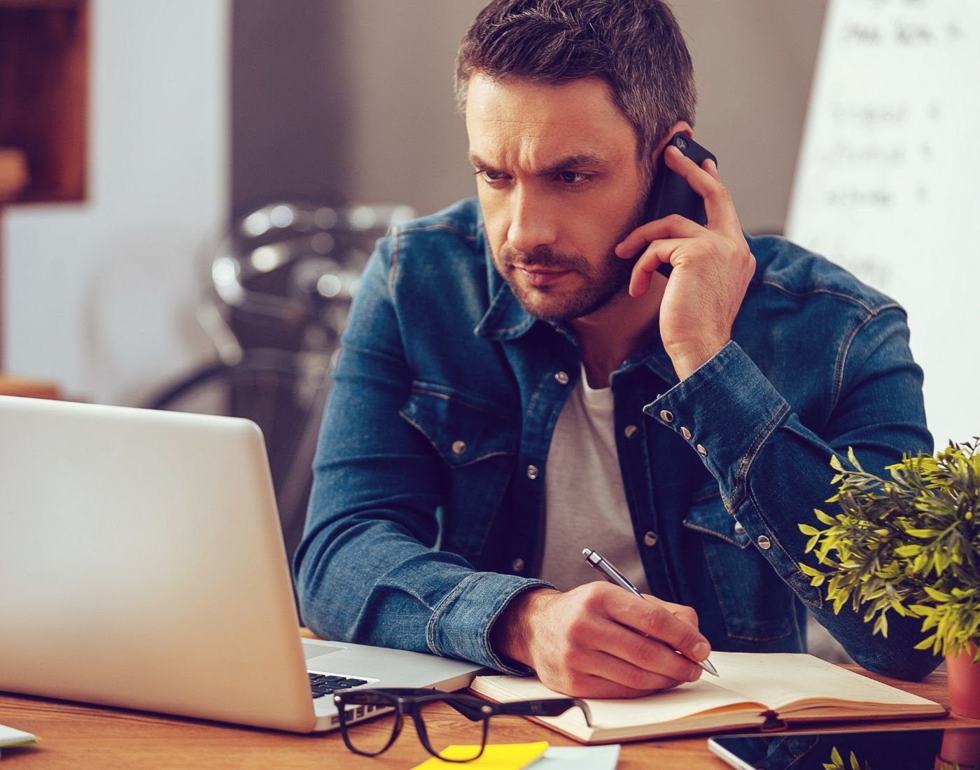 Man with a beard looking at a laptop screen. He's also on the phone.