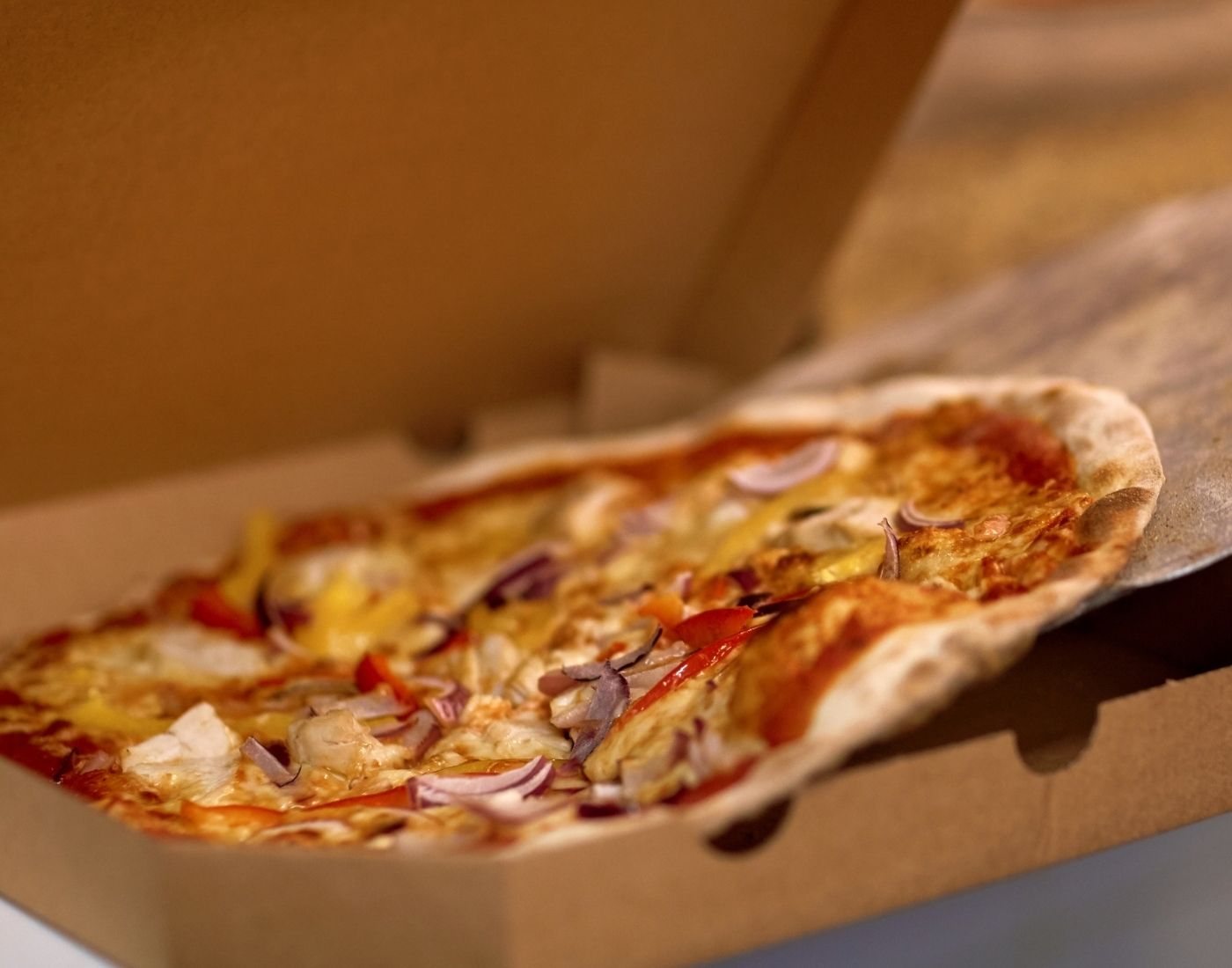 A pizza with melted cheese, onion, and other toppings in an open cardboard box.