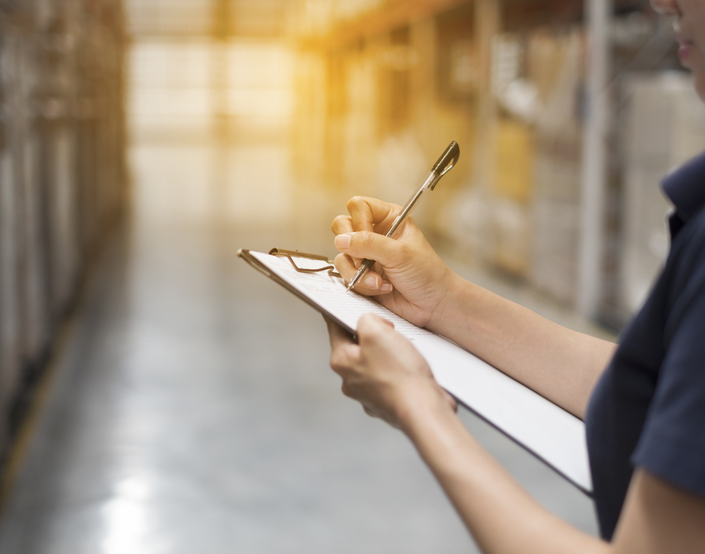Female hand writes something on a clip board in a standard warehouse