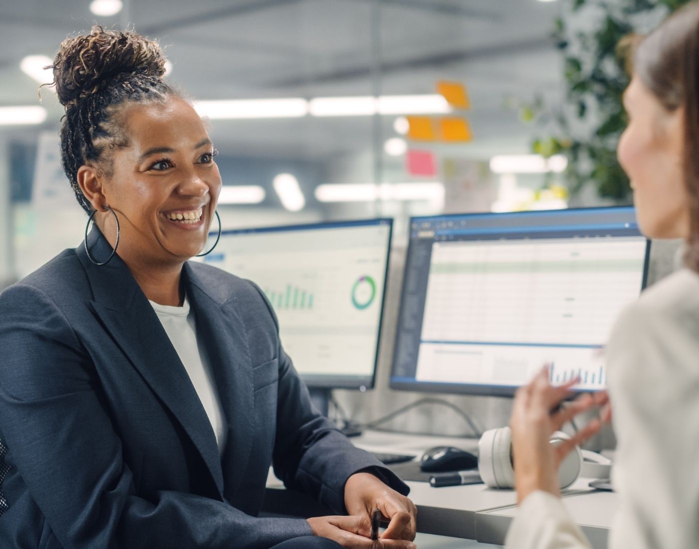 Two female colleagues have a conversation. One is smiling and the other has her back to the camera.