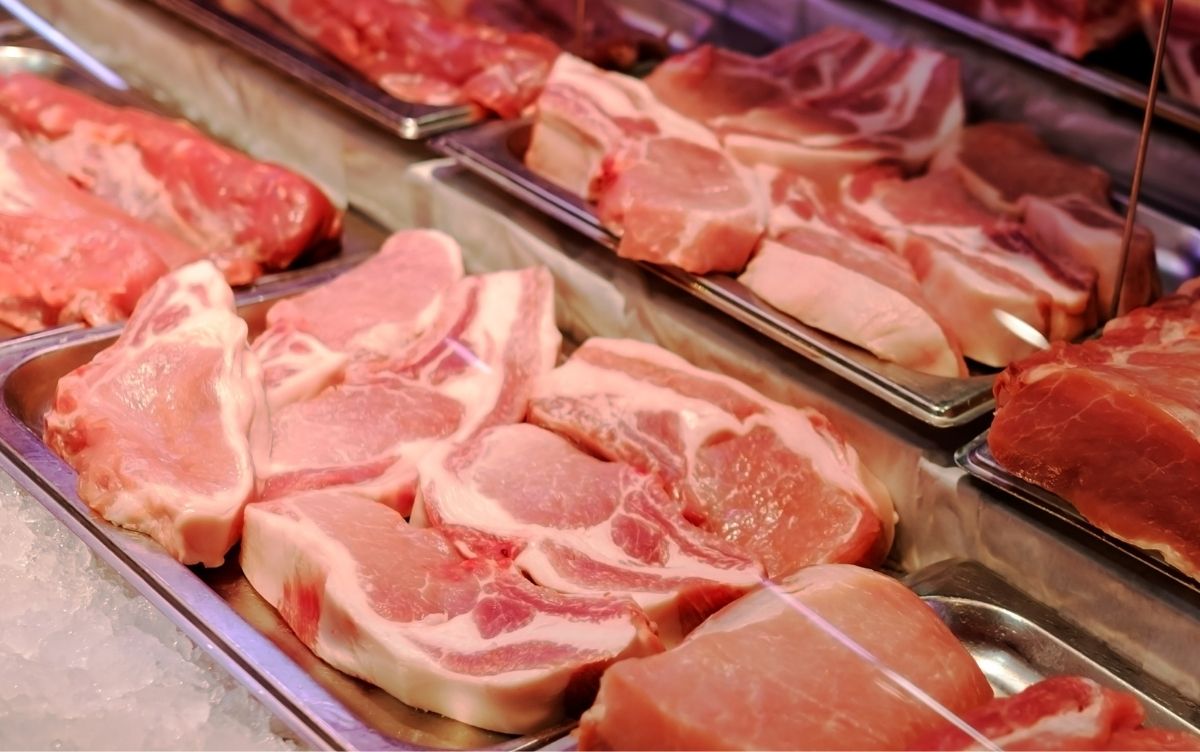 Raw pork cuts displayed on trays in a well-lit supermarket or butcher shop.