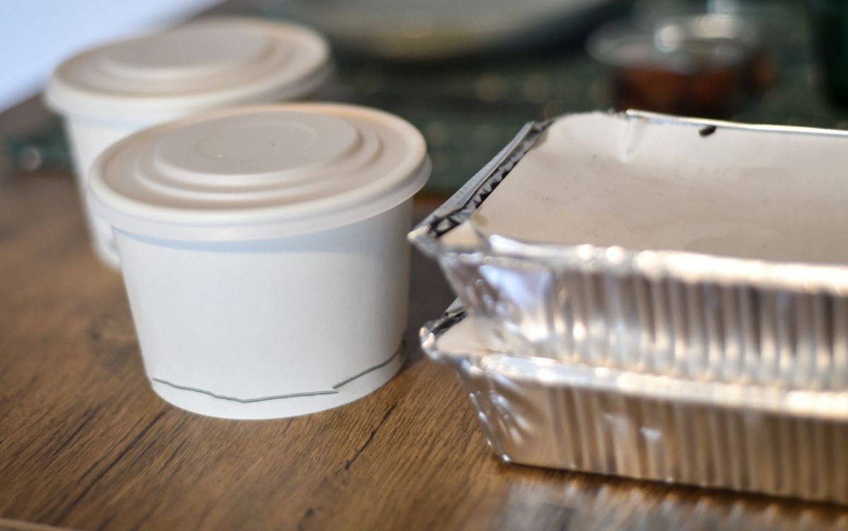 Two white takeout containers and a metallic takeaway tray on a wooden table