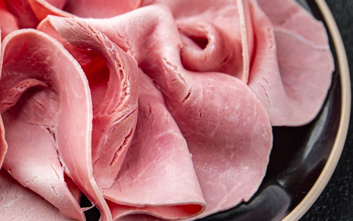 Slices of pink ham neatly arranged on a black plate with a gold rim.