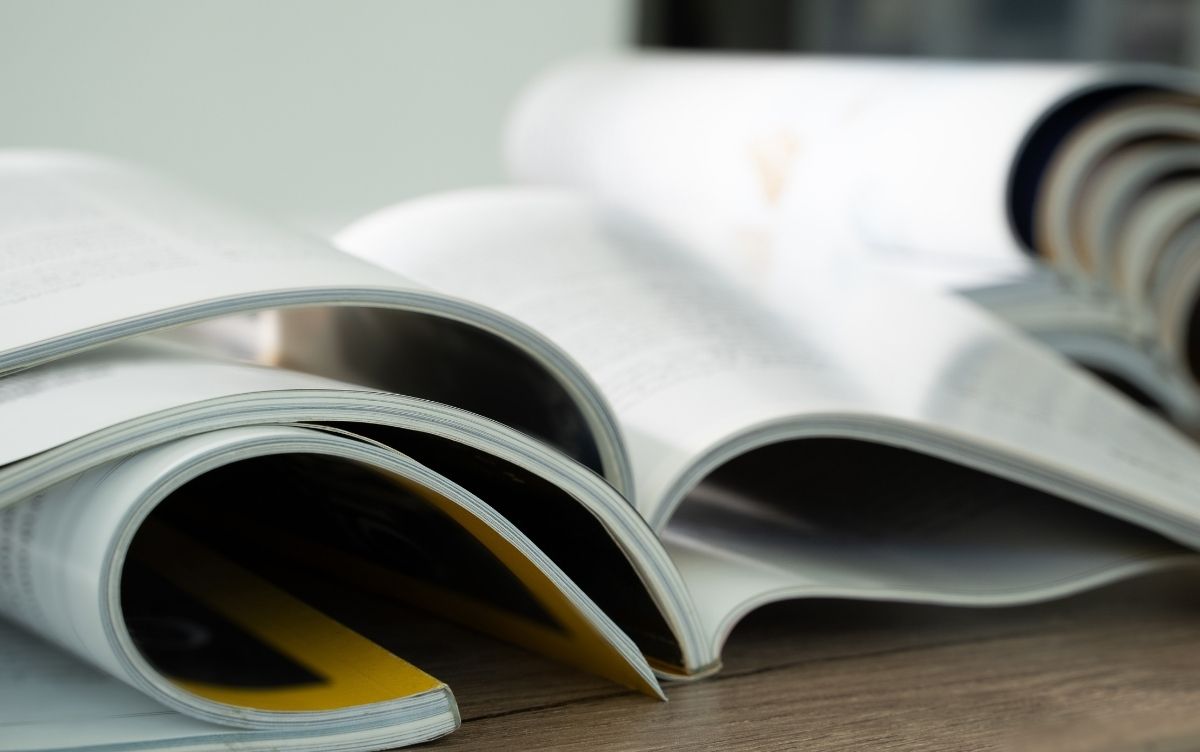 Several open magazines overlapping on a wooden surface, showcasing glossy pages and varied content in a casual reading arrangement.