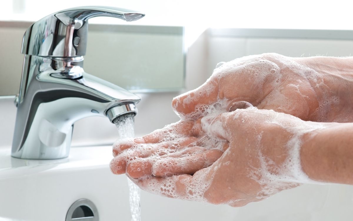 A person washing hands with soap under running water from a faucet.