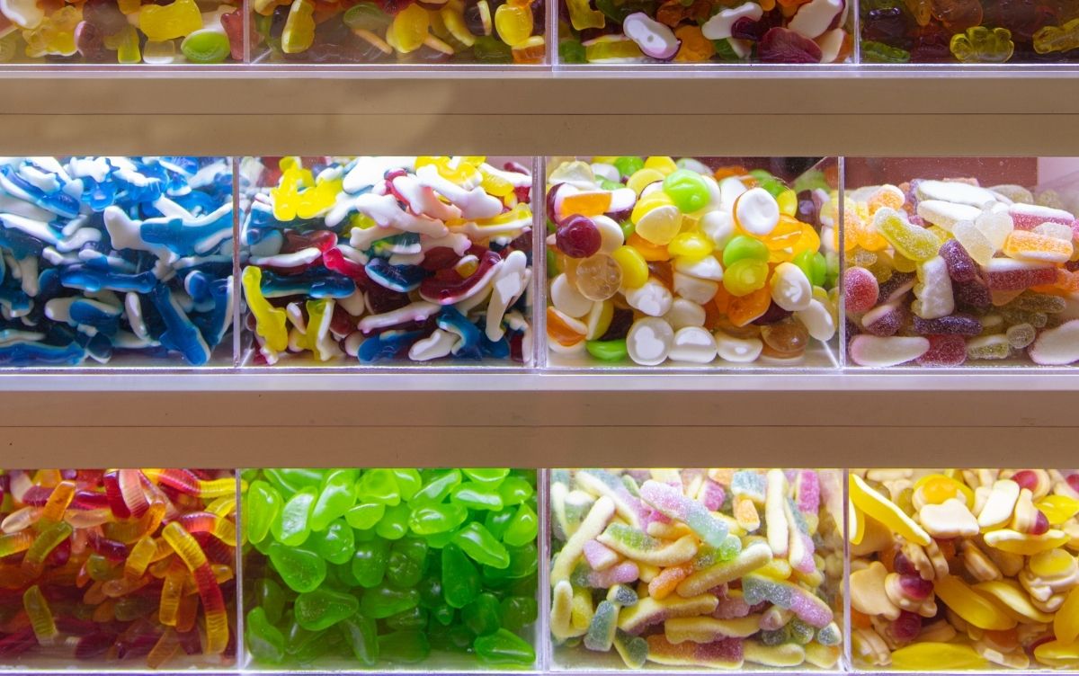 Variety of colorful candies displayed in clear bins, including gummy sharks, jelly beans, and fruit slices.