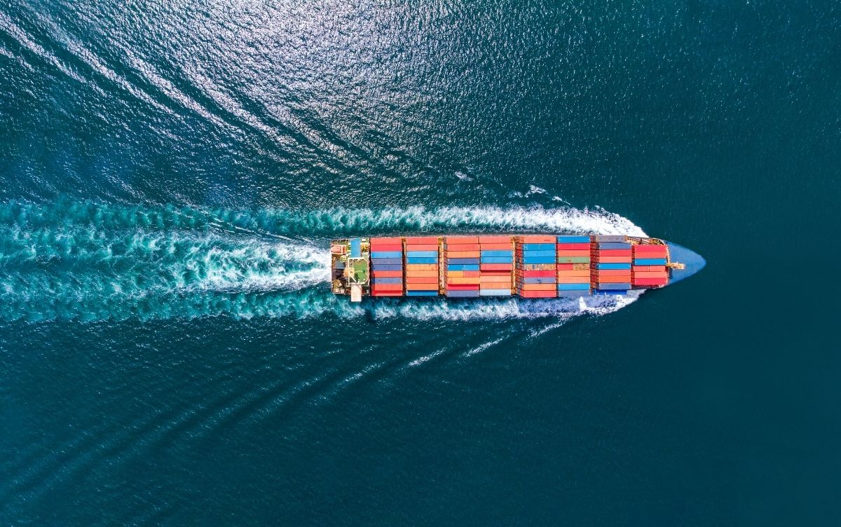 Aerial view of a large cargo ship carrying multiple colored containers, sailing through blue ocean waters.