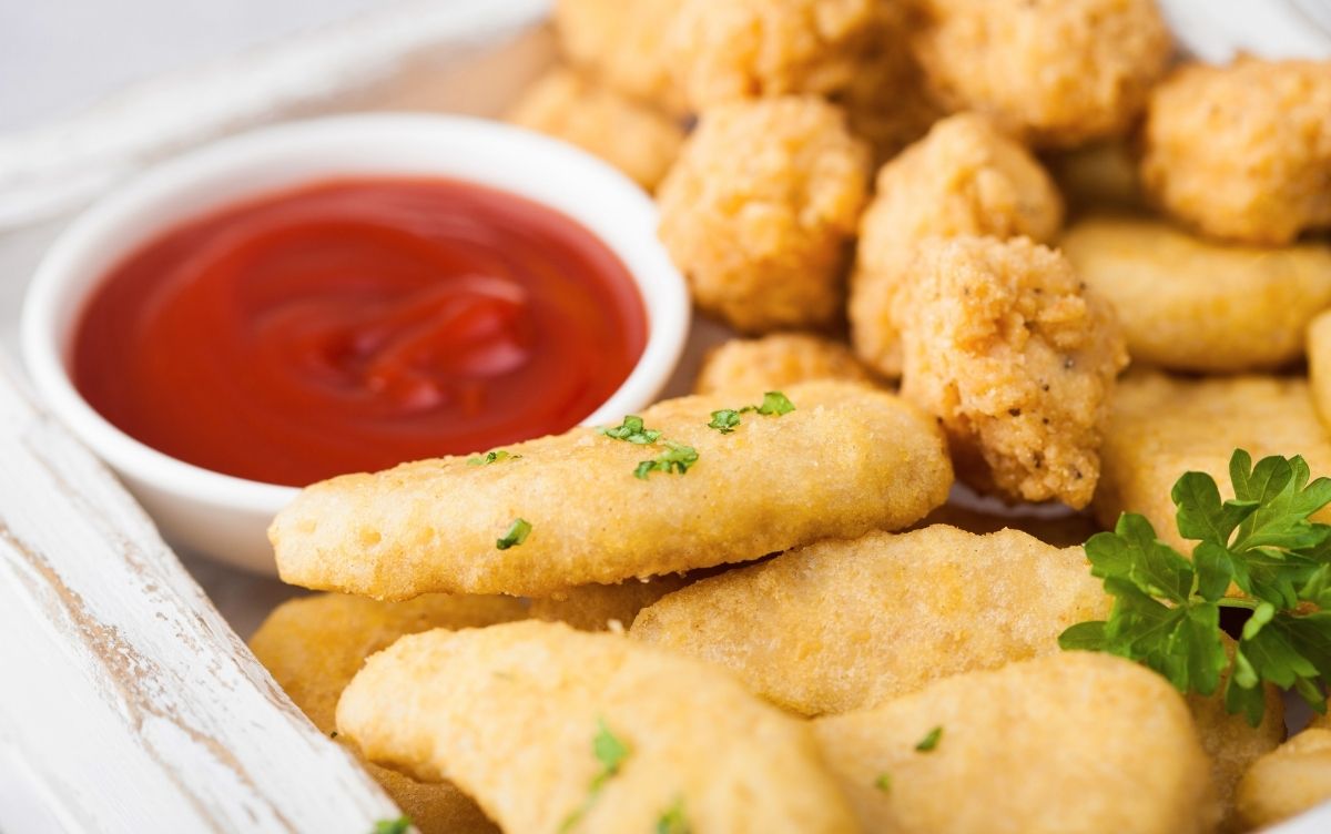 Chicken nuggets, popcorn bites and ketchup on a plate.