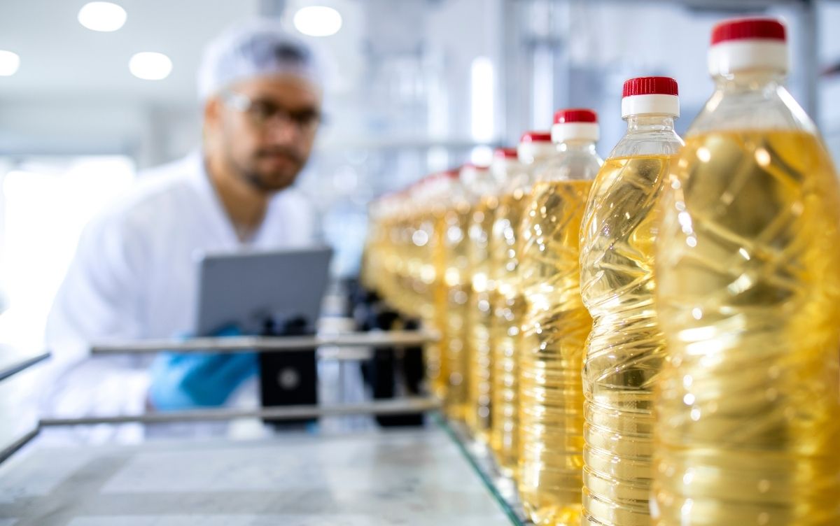 Quality control worker inspecting bottles of cooking oil on a production line in a factory.
