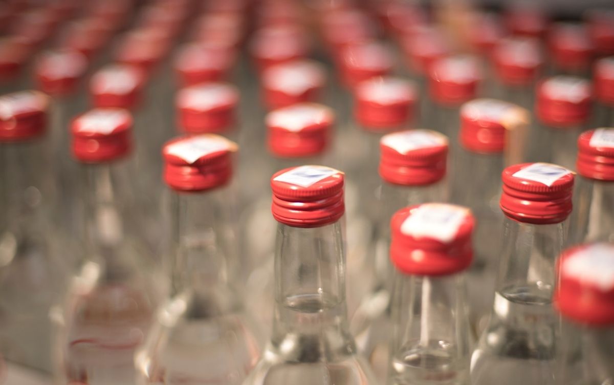 Rows of glass bottles containing clear alcoholic spirits with red caps