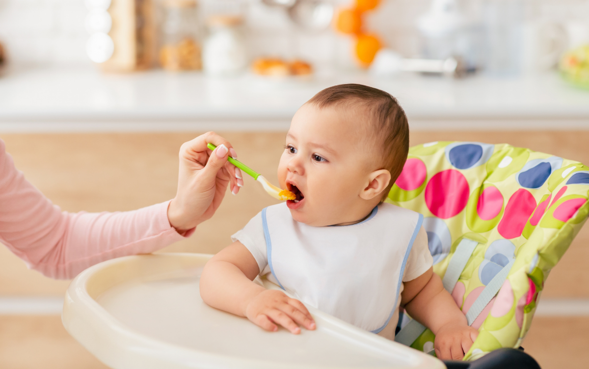 a baby is given food from a spoon whilst sitting in a high chair