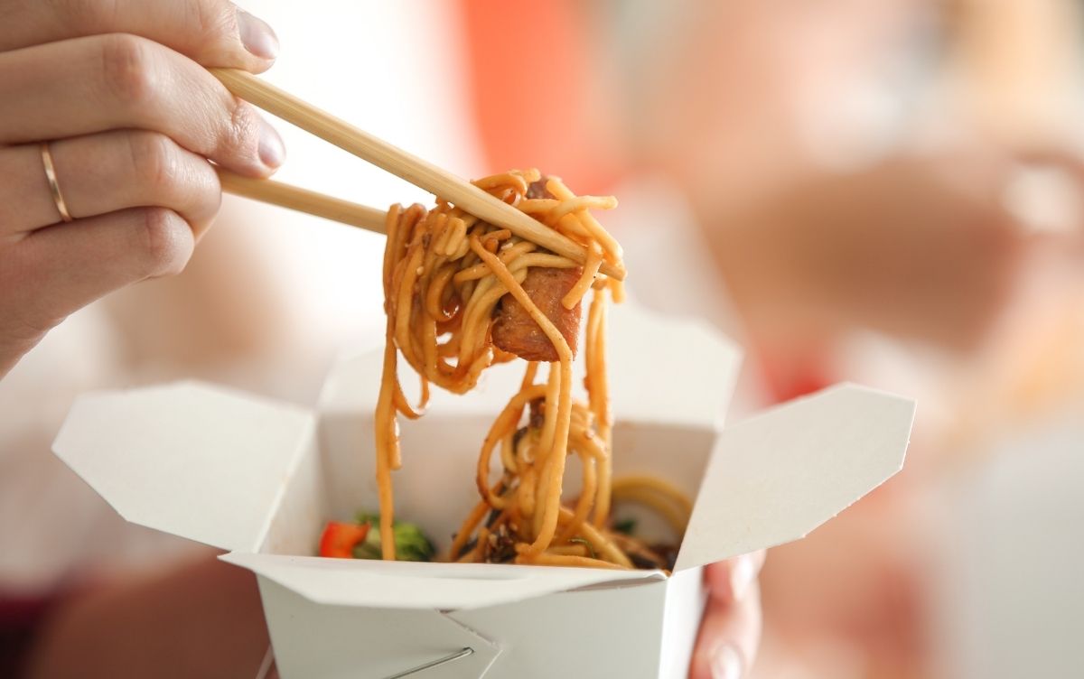 A person uses chopsticks to lift noodles from a takeout box.