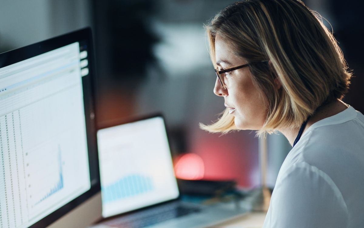 Female researcher sitting at a desk looking at a computer. The computer screen has data displayed on it.