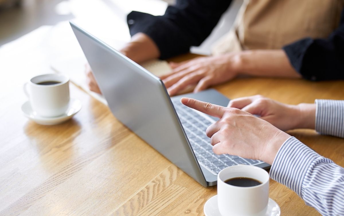 Two hands pointing at a laptop.