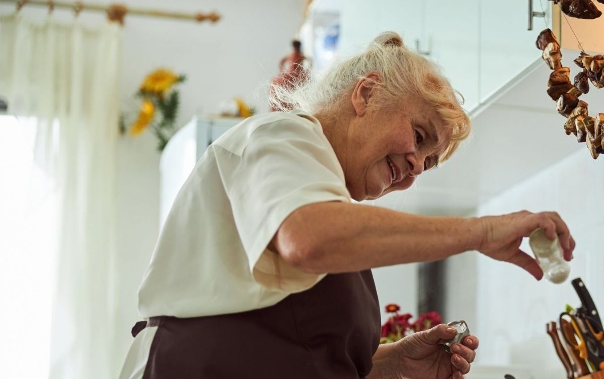 Women with white hair aged over 65. She's standing at an over and pouring salt.
