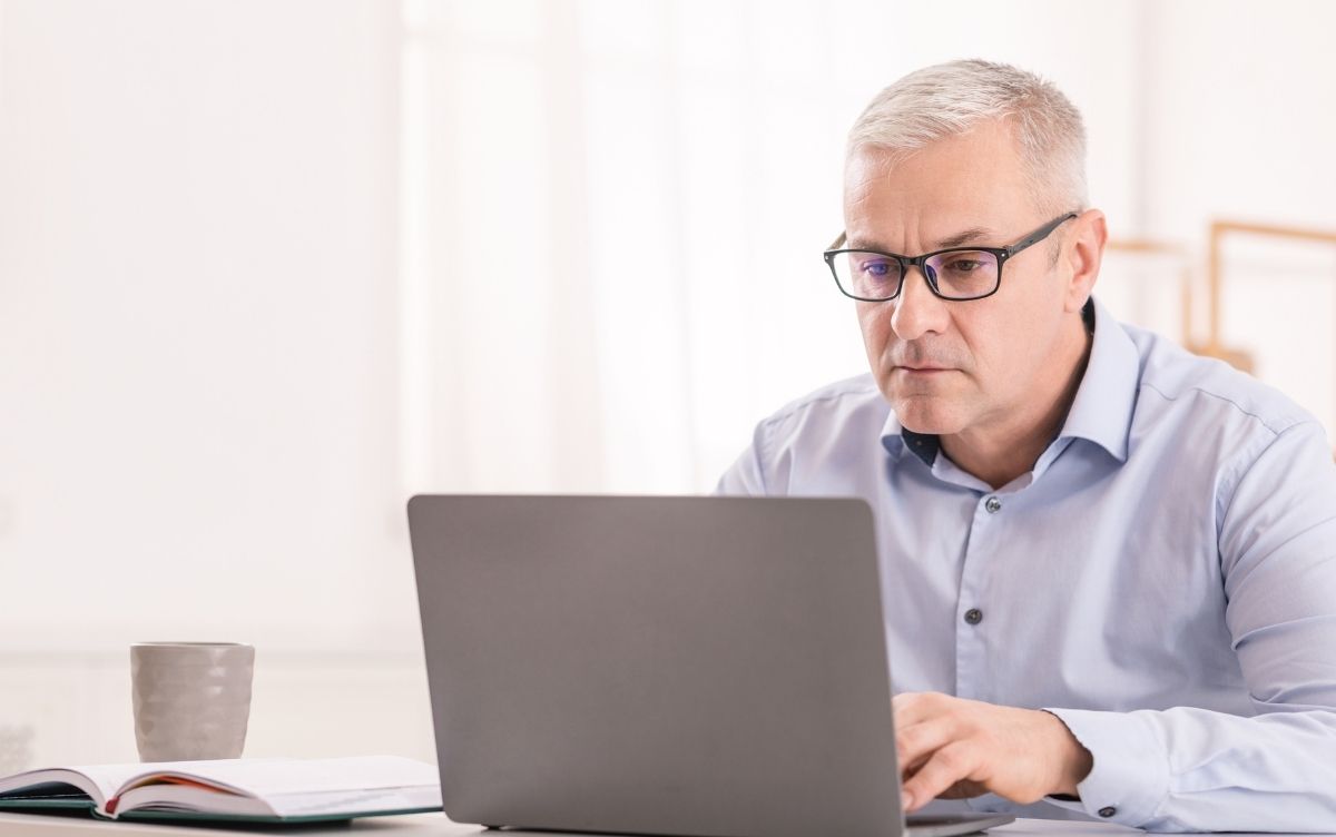 Man in his fifties sitting at his laptop. He has a serious look on his face.