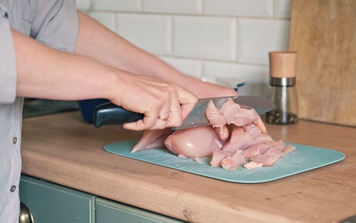 map chopping raw chicken on a chopping board at home