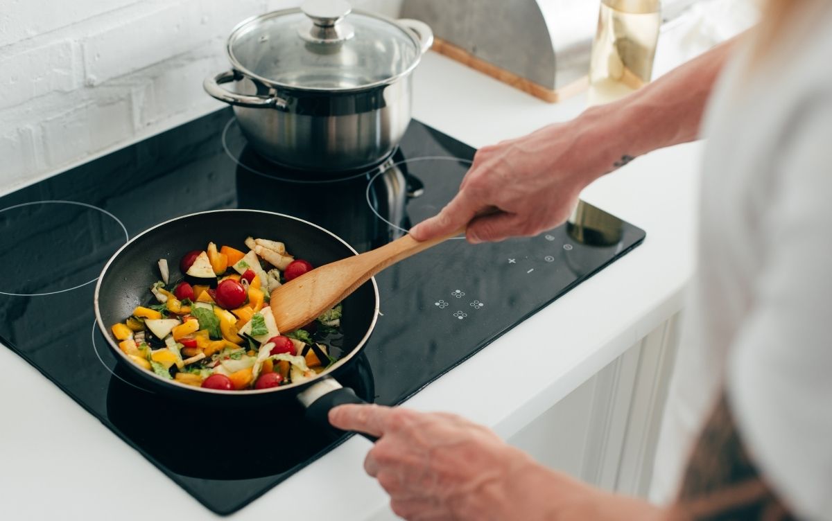 Person cooking coluorful vegetables in a frying pan on a modern stovetop.